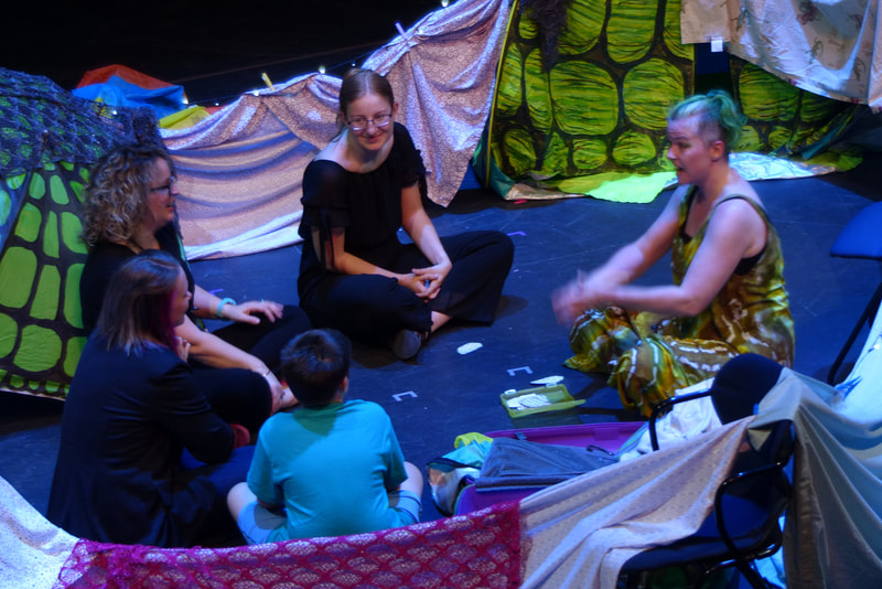 A group of peope sit talking in a blanket fort.